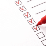 A red pen is being used to mark a check mark on a checklist in the context of marketing tasks.