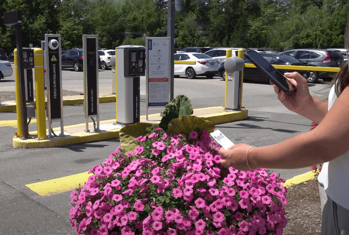 A woman is holding a cell phone near a flower pot, showcasing the seamless integration of parking and mobility solutions.
