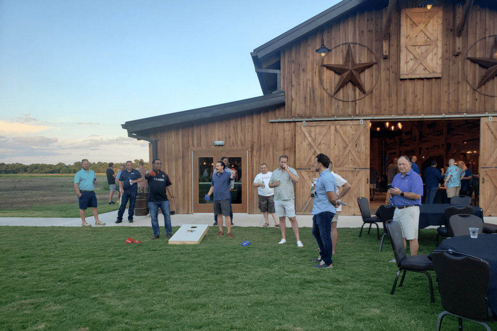 Members of the Texas Parking & Transportation Association enjoying a game of corn hole in front of a rustic barn.
