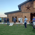 Members of the Texas Parking & Transportation Association enjoying a game of corn hole in front of a rustic barn.