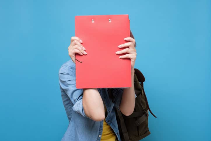 A girl in a situation covering her face with a red folder, expressing her emotions.