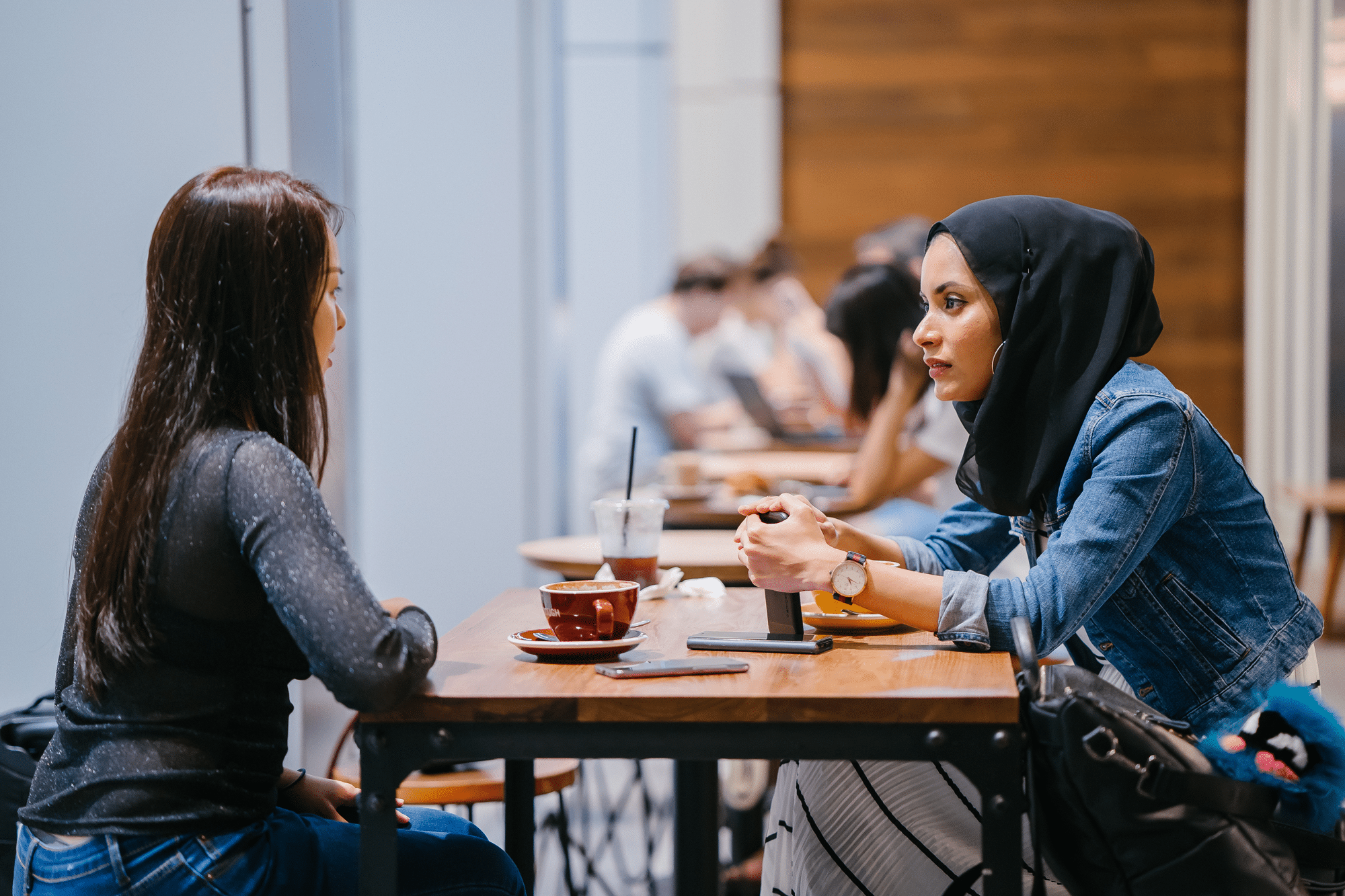 Two Muslim women engaging in conversation at a coffee shop, highlighting diversity and inclusion.