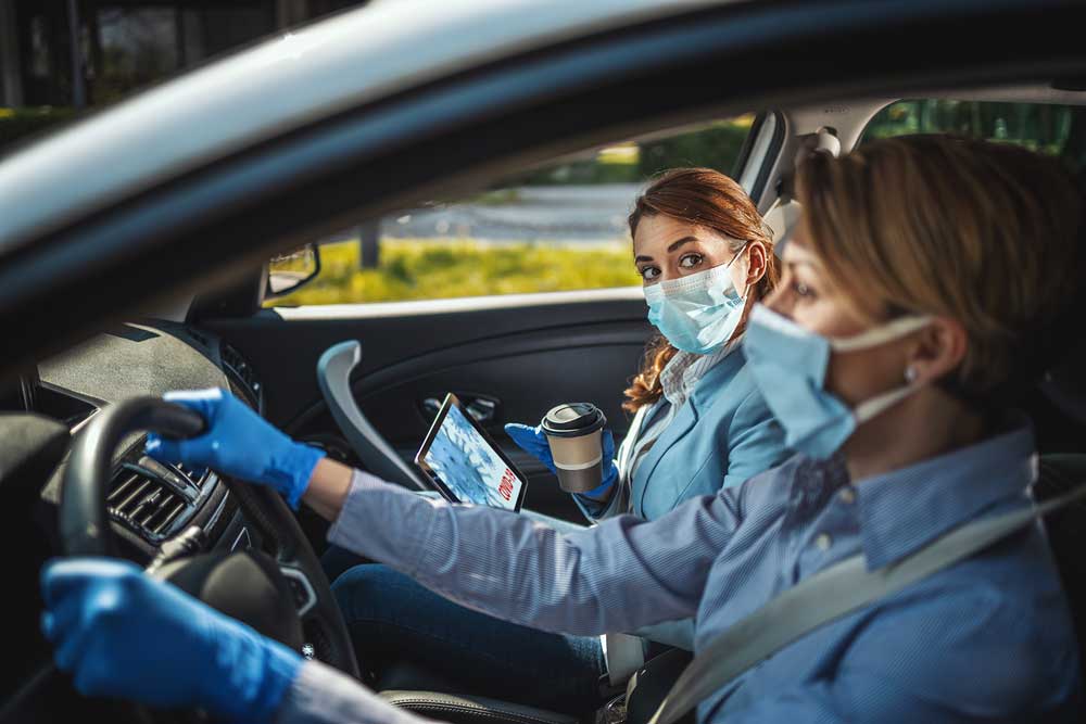 Two business women driving in the car with masks on