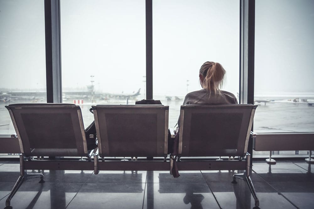 An important woman sits on a bench looking out a window at an airport.