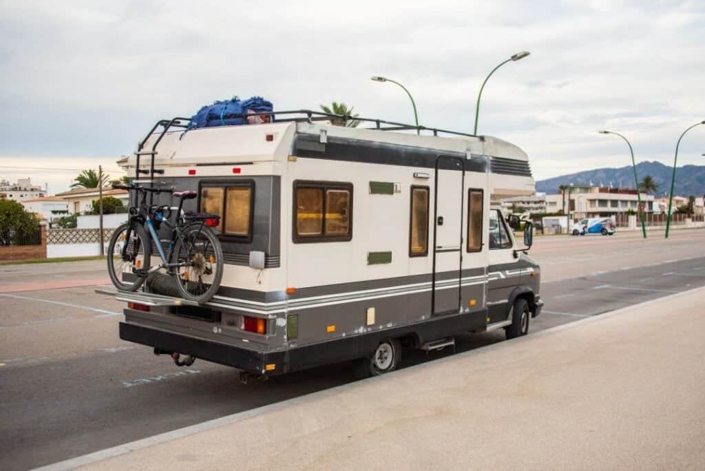 An inhabited RV parked on the side of the road with a bicycle on top.