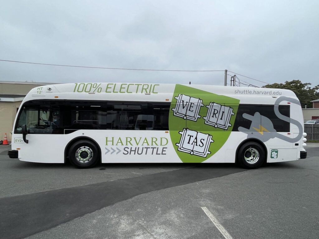 The Harvard shuttle, an electric bus, is parked in a parking lot.