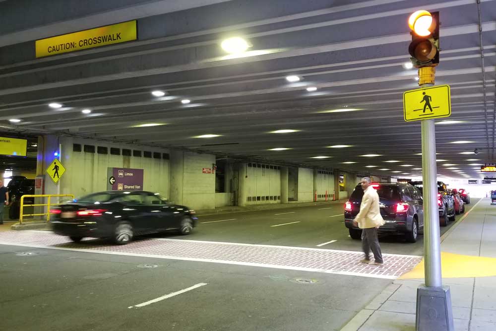 black man walking across crosswalk in parking garage with car not stopping