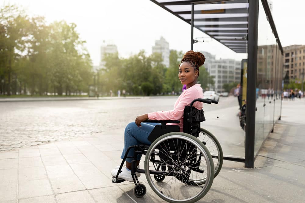 Young black handicapped woman in wheelchair cannot board vehicle suitable for impaired persons, waiting on bus stop
