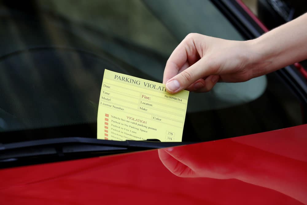 Close up of person taking a yellow parking ticket off of their windshield