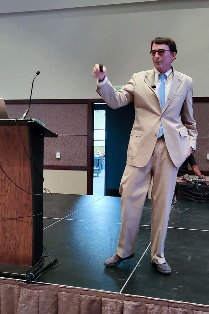 A man in a tan suit standing on a stage at a regional event.