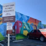 photo of a sign that says Downtown Parking Permit required, in front of a parking lot and colorfully painted building