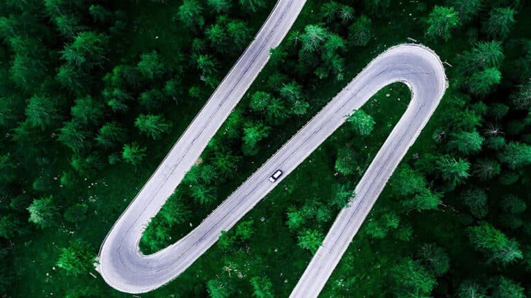 Arial photo of winding road through a vibrant green forest with a single vehicle