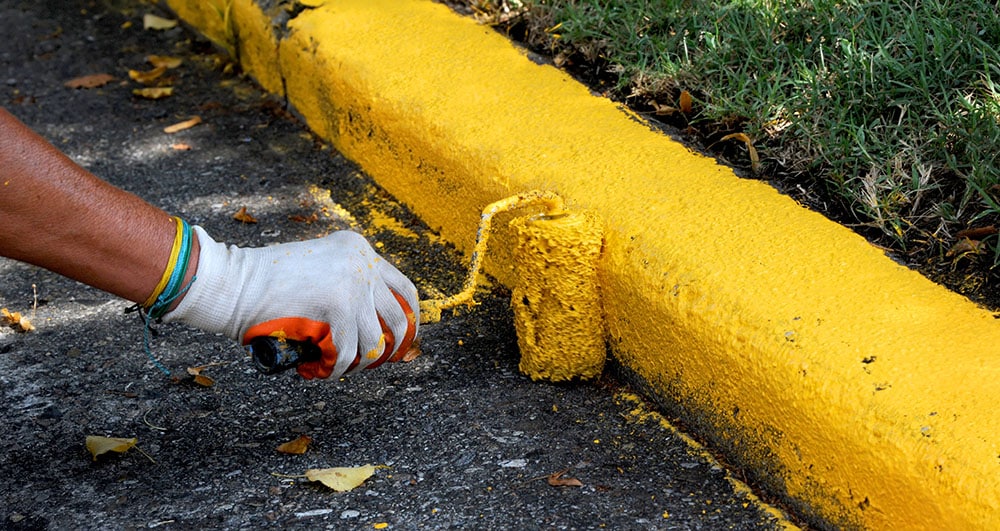 Person painting a curb yellow
