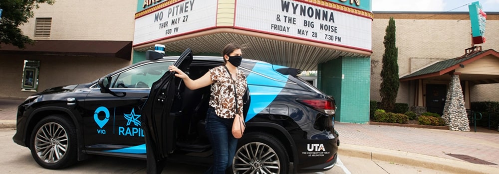 A woman standing next to a black car in front of a theater in the context of a Smart City.