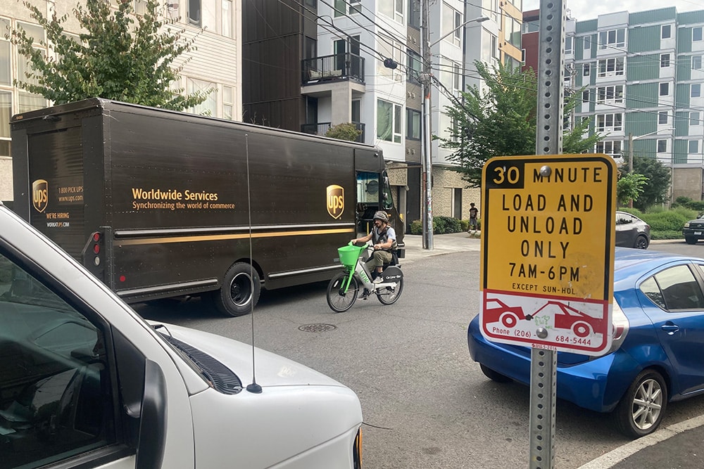 Photo of a UPS truck, cyclist and parked cars all sharing the street in a loading zone