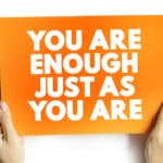 Hands holding and orange sign that reads "You Are Enough Just As You Are"