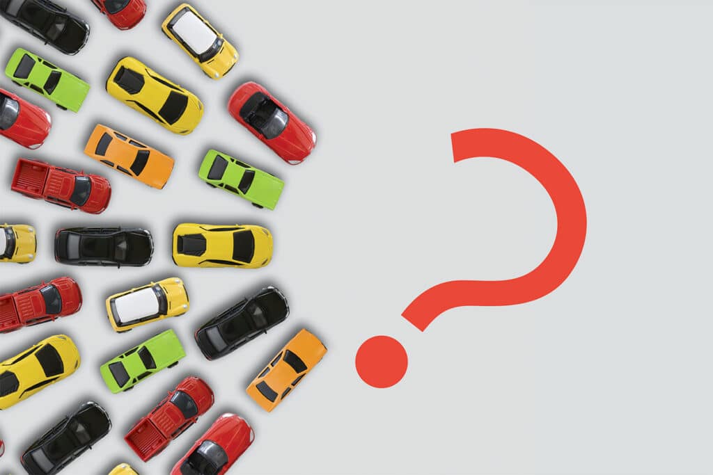 An overhead view of toy cars lined up around a question mark.