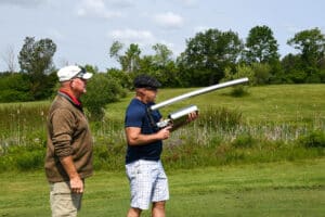 Two men standing on a golf course. Ben Fletcher (right) is aiming a "golf cannon" down the course.