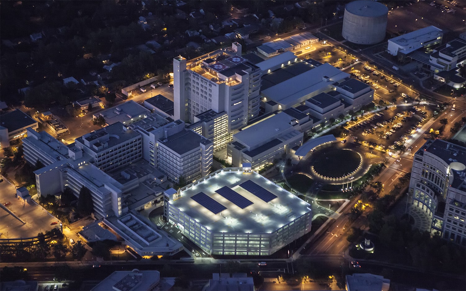 Aerial view of UC Davis Medical Center at night, illuminated buildings and streets bustling with activity.