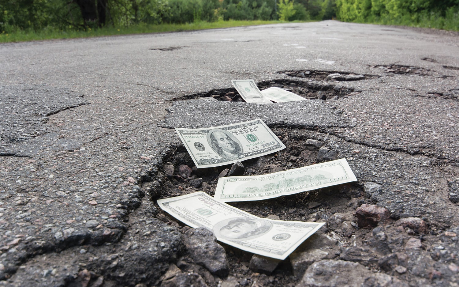 Cracked asphalt with scattered $100 bills.