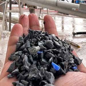Hand holding plastic asphalt pieces with construction work in the background.