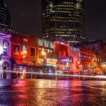 Nighttime Nashville street with vibrant neon signs and wet pavement.