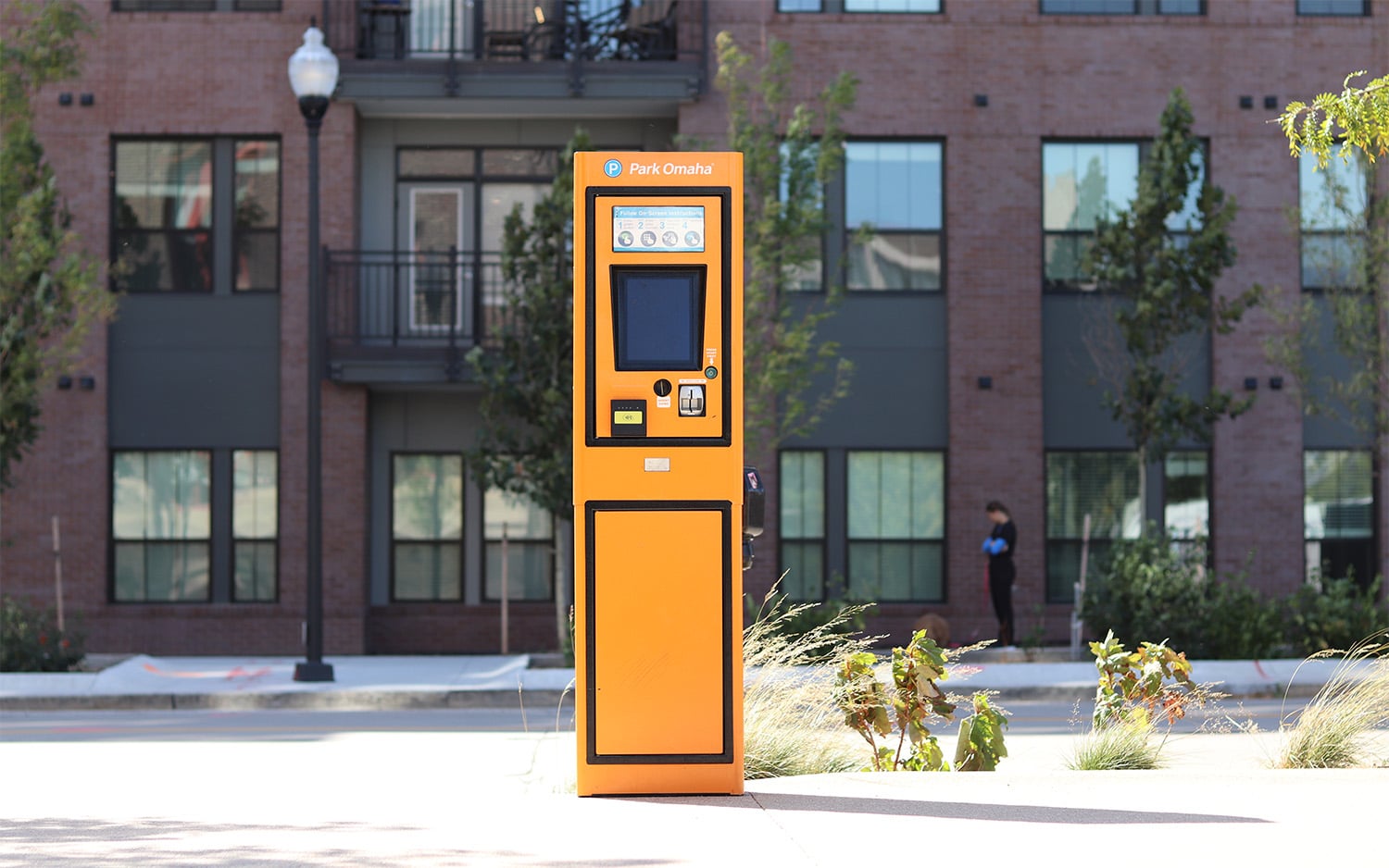 Orange parking meter on a sidewalk with urban backdrop.