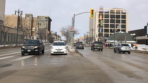 A city street with vehicles driving down it, monitored by the Winnipeg Parking Authority.