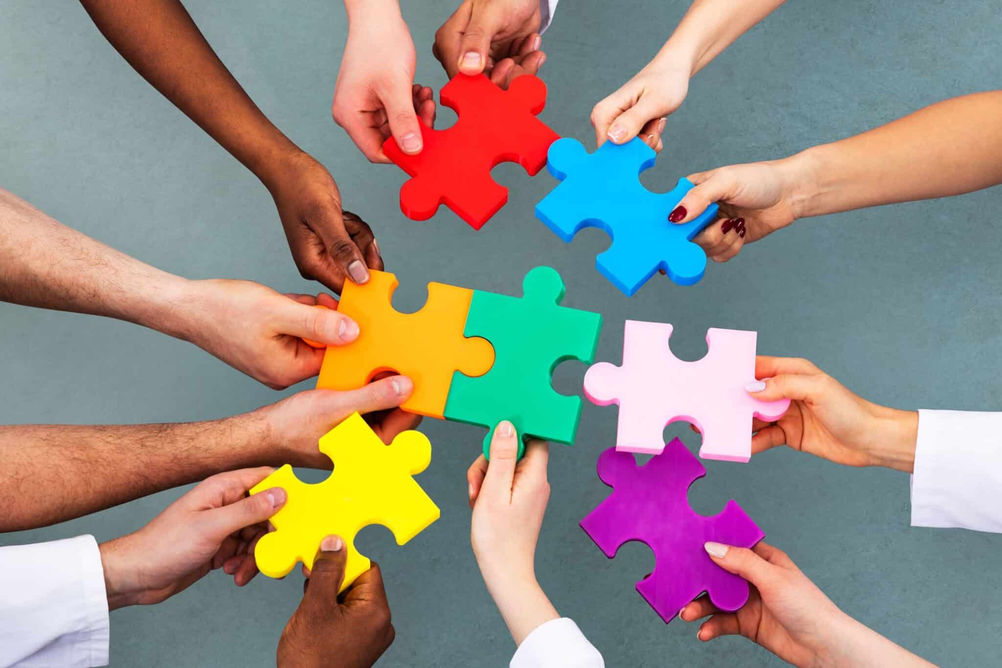 A diverse group of people promoting inclusivity by holding colorful puzzle pieces together.