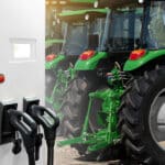 A green tractor is plugged into an electric charging station.