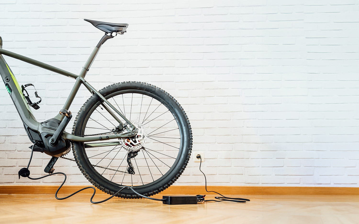 A bicycle is parked in front of a white wall and plugged into an outlet.