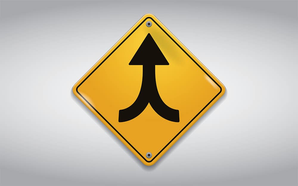 A yellow road sign indicating a merger with an arrow pointing in the opposite direction.