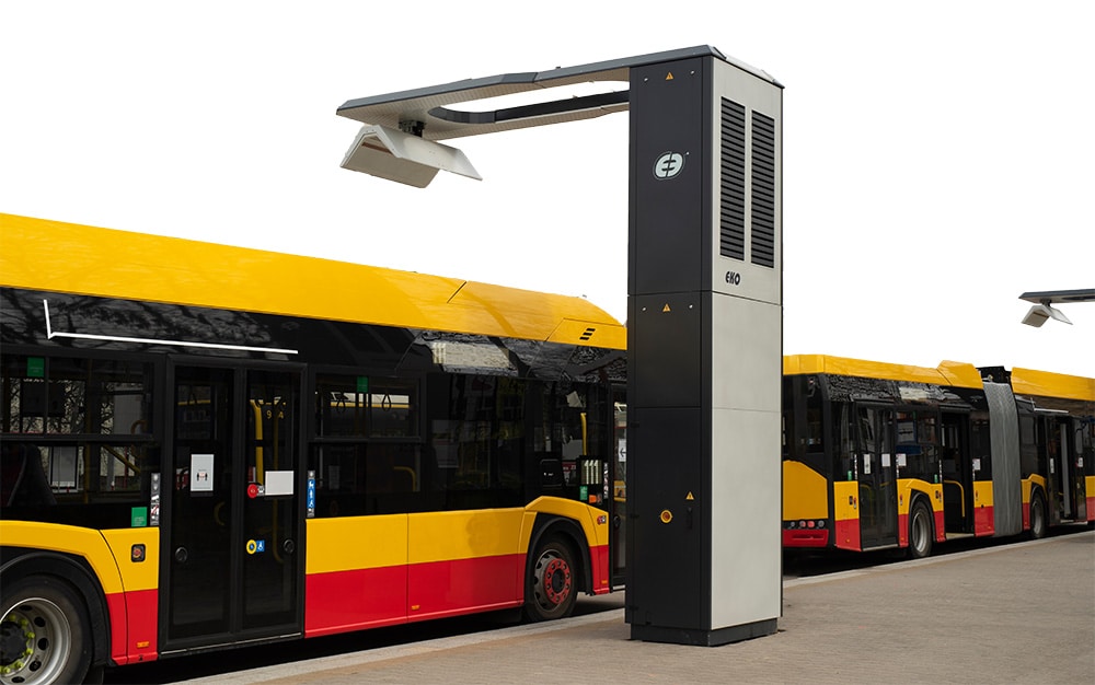 A group of yellow and red buses parked under wireless charging stations.