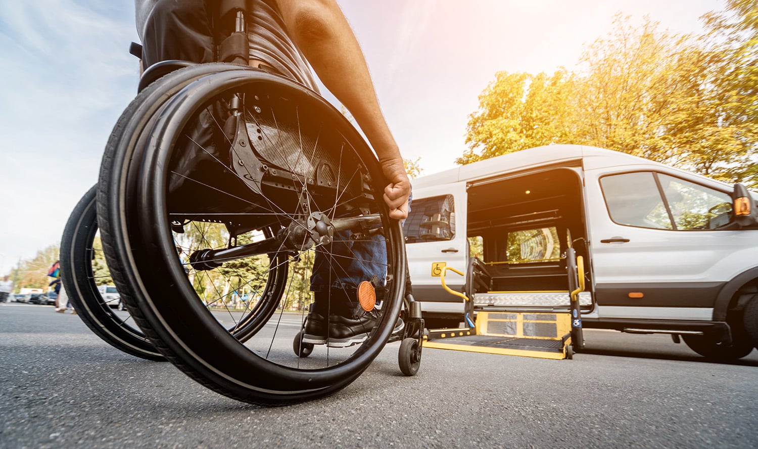 A person in a wheelchair approaches an accessible van with an open ramp on a sunny day.
